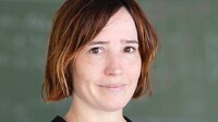 Dr. Maia Verginory mit kurzem Haar, vor einer Schultafel, freundlich blickend.